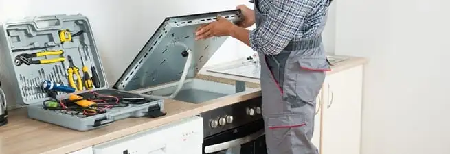 Cooktop repair technician lifting a built-in stovetop for service in Overland Park, KS