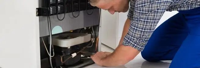 Refrigerator repair technician servicing the compressor and condenser area in Overland Park, KS