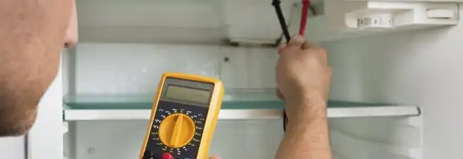 Refrigerator repair technician testing electrical components with a multimeter in Overland Park, KS