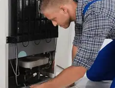 Refrigerator repair technician servicing the compressor and condenser area in Overland Park, KS