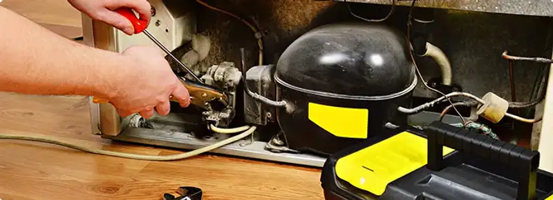 Refrigerator repair technician fixing the compressor and wiring in Overland Park, KS